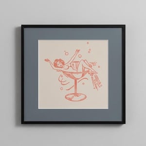 Puede incluir: Lámina enmarcada con una ilustración retro de una persona reclinada en una gran copa de cóctel. La obra de arte es de estilo minimalista, con un diseño de color coral sobre un fondo crema. La impresión está enmarcada en negro.