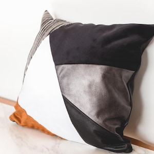 Peut inclure: Un coussin décoratif avec un design géométrique. Le coussin présente un patchwork de matériaux en noir, blanc, argent et marron. La partie supérieure est en velours noir et le bas en cuir noir.