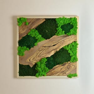 Op de afbeelding: Vierkante wandkunst met houten frame met een natuurlijk ontwerp. Het kunstwerk bevat donkergroen mos, felgroene mosaccenten en delen van lichtbruin hout. Het ontwerp is een mix van natuurlijke texturen en kleuren.