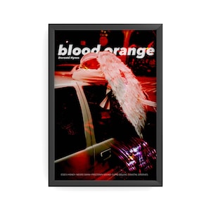 May include: A framed art print with the words "blood orange" and "Devonté Hynes". The image depicts a person with white angel wings resting on a car. The print's base lists album titles: Essex Honey, Negro Swan, Freetown Sound, Cupid Deluxe, Coastal Grooves.