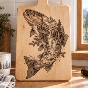 May include: A light-colored wooden cutting board featuring a detailed laser-engraved illustration of a large fish. Inside the fish silhouette is a scenic landscape showing a person fly fishing in a river surrounded by pine trees and mountains.