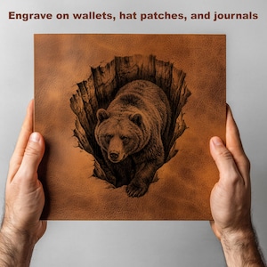 K&ouml;nnte beinhalten: Ein braunes Lederquadrat mit einer detaillierten Gravur eines Grizzlyb&auml;ren, der aus einer Spalte auftaucht. Der Text "Engrave on wallets, hat patches, and journals" steht oben. Das Quadrat wird von zwei H&auml;nden gehalten.