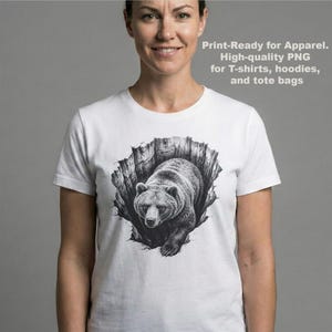 K&ouml;nnte beinhalten: Wei&szlig;es T-Shirt mit einer schwarz-wei&szlig;en Illustration eines B&auml;ren, der aus einer zerfetzten Oberfl&auml;che kommt. Der Text "Print-Ready for Apparel. High-quality PNG for T-shirts, hoodies, and tote bags" ist auf dem T-Shirt aufgedruckt.