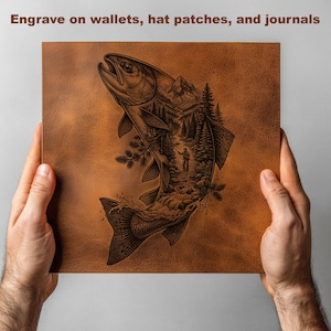 May include: A square piece of tan leather featuring a dark laser-engraved illustration of a jumping fish with a forest, mountain, and angler scene inside its body. The text Engrave on wallets, hat patches, and journals is at the top.