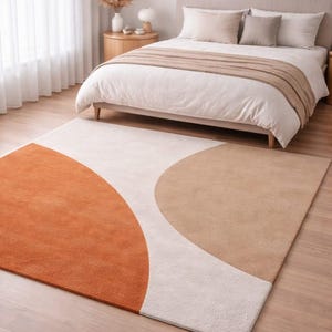May include: A modern area rug with a geometric design in shades of orange, beige, and white. The rug is rectangular and features curved shapes, adding a contemporary touch to the bedroom setting. The rug is placed on a wooden floor.