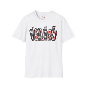 May include: White t-shirt featuring the word "Vandals" in a graffiti-style font. The text is outlined in black with a red, black, and white plaid pattern filling the letters. The shirt has a crew neck and short sleeves.