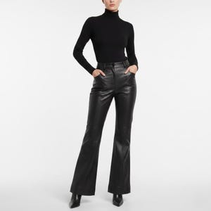 Puede incluir: Una persona con un top negro de cuello alto y pantalones de cuero negros. Los pantalones tienen un diseño de pierna acampanada y se combinan con zapatos negros de punta. El conjunto está sobre un fondo blanco.