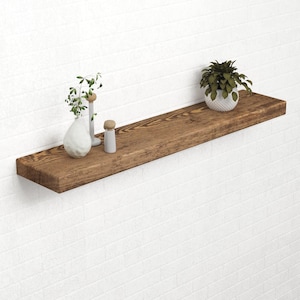 Peut inclure: Étagère flottante en bois brun foncé, fixée à un mur de briques blanches. Elle présente un vase blanc avec de la verdure, un petit objet décoratif et une plante en pot. L'étagère mesure environ 122 cm de long.