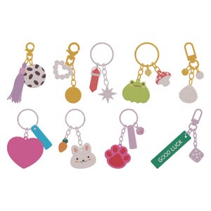 May include: A selection of keyrings with diverse charms. Designs include a polka-dot ball with a tassel, a yellow circle with white beads, a red crystal, a star, a green frog, a mushroom, a pink heart, a carrot, a bunny, a paw print, a dice, and a tag that says "GOOD LUCK".