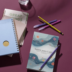 May include: A collection of notebooks, pens, and a glass of water on a purple surface. The notebooks include a light blue spiral-bound notebook with a gold circle, a notebook with the text "GREAT THINGS", and a book titled "Nutrir para Cuid-".