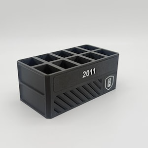 May include: A black rectangular organizer with multiple compartments. The front of the organizer has the number "2011" in white text, along with a white logo. The sides have a textured design.