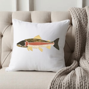 May include: A square white throw pillow featuring a centered graphic illustration of a fish. The fish design incorporates textured patterns in shades of olive green, dark brown, cream, and a prominent horizontal stripe of muted terracotta orange.