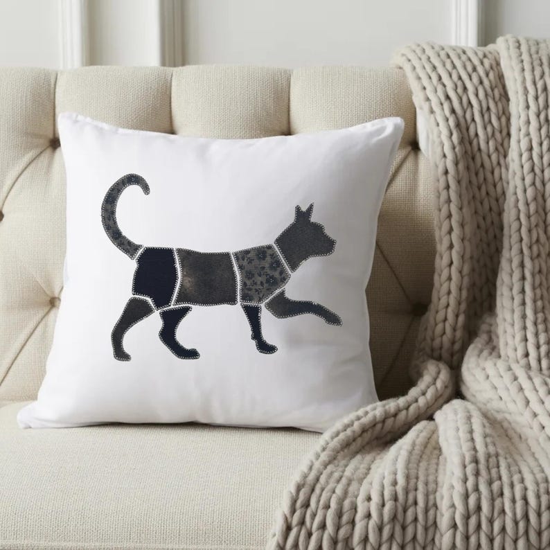 May include: A square white throw pillow featuring a dark gray cat silhouette in the center. The cat design is divided into several distinct sections with visible stitching, showcasing different shades and textures of gray and black fabric patterns.
