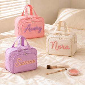 May include: Three rectangular quilted cosmetic bags with top handles and zippered closures. The pink bag features the name Avery in purple, the cream bag features Nora in pink, and the purple bag features Sienna in yellow. Two makeup brushes and a blush compact.