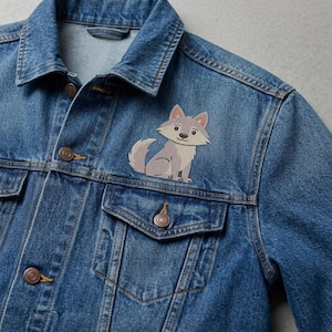 May include: A blue denim jacket featuring a stitched patch of a cartoon wolf. The wolf is light gray with darker gray accents, pink inner ears, and a bushy tail. The jacket has a classic collar, metal buttons, and two chest pockets with flaps.