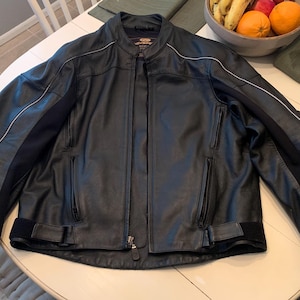 May include: Black leather motorcycle jacket with a stand-up collar, zipper closure, and white accent stripes on the sleeves. Features zippered pockets and adjustable waist straps. A classic, protective outerwear garment.