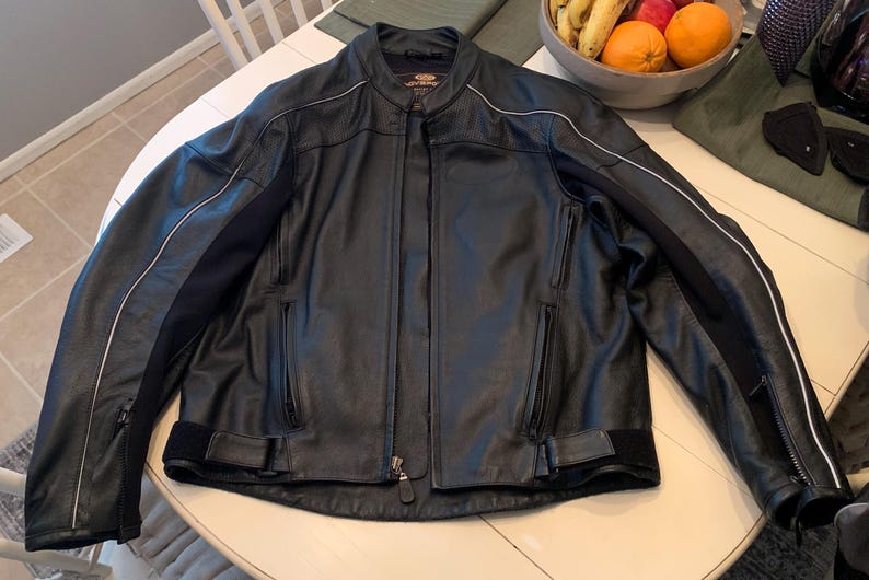 May include: Black leather motorcycle jacket with a stand-up collar, zipper closure, and white accent stripes on the sleeves. Features zippered pockets and adjustable waist straps. A classic, protective outerwear garment.