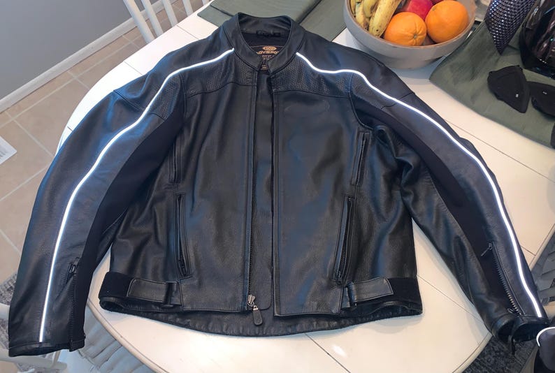 May include: Black leather motorcycle jacket with white reflective stripes on the sleeves and shoulders. The jacket has a zippered front, pockets, and a stand-up collar. A classic piece of outerwear.