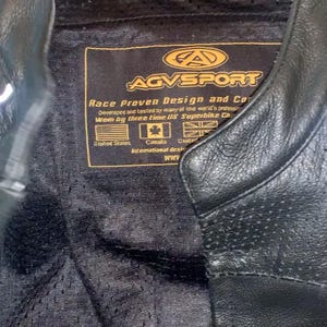 May include: Black leather motorcycle jacket with a perforated inner lining. The jacket features a label with the text "AGVSPORT Race Proven Design and Co." and flags of the United States, Canada, and the United Kingdom.