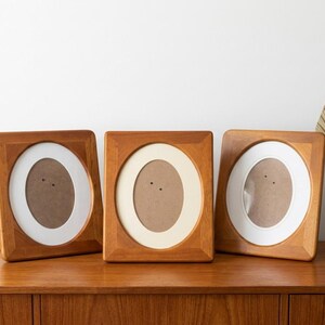 May include: Three rectangular wooden picture frames with rounded oval inner cutouts. Each frame features a light brown wood grain finish and includes a white mat board surrounding the central oval opening for displaying photographs or artwork.