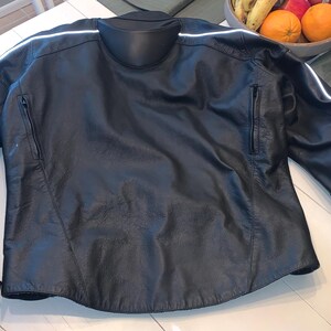 May include: Black leather motorcycle jacket with a mandarin collar and zippered pockets. Features white reflective stripes on the sleeves and shoulders. A classic design for motorcycle enthusiasts.