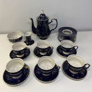 Puede incluir: Juego de té azul marino con detalles dorados. El conjunto incluye una tetera, tazas, platillos, azucarero, candelabro y calentador. Las tazas y platillos presentan un diseño de hojas doradas.