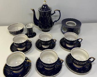 May include: A complete navy blue tea set with gold accents. The set includes a teapot, cups, saucers, a sugar bowl, a candle holder, and a warmer. The cups and saucers have a delicate gold leaf pattern.