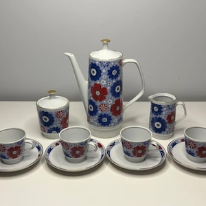 Puede incluir: Juego de café de porcelana vintage con fondo blanco y estampado floral azul y rojo. El juego incluye cafetera, lechera, azucarero y seis tazas con platillos. La cafetera mide aproximadamente 25 cm de altura.