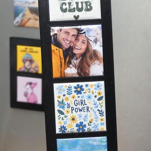 May include: A black framed magnetic photo display featuring four square tiles. The top tile reads "SELF LOVE CLUB" with floral accents. The second tile has a photo of a smiling couple. The third tile says "GIRL POWER" with floral designs. The bottom tile shows a blue water scene.