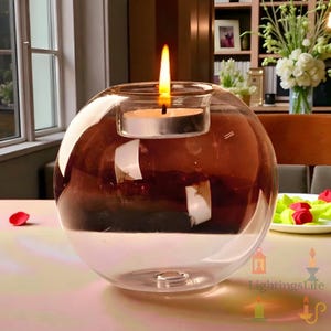 Op de afbeelding: Een heldere glazen kandelaar met een bruine tint, met een brandende waxinelichtkaars. De bolvormige houder staat op een tafel, met een zachte gloed die van de vlam uitgaat. De kandelaar is een decoratief item.
