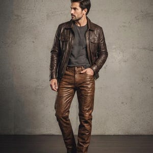 Peut inclure: Veste en cuir marron avec deux poches poitrine et pantalon en cuir marron assorti. La tenue est associée à un t-shirt gris et des chaussures en cuir marron. Le modèle se tient devant un mur en béton gris.