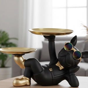 Könnte beinhalten: Schwarze Bulldoggen-Figur mit goldenen Akzenten, Sonnenbrille und Fliege, die zwei goldene Tabletts hält. Diese dekorative Skulptur ist ein einzigartiges Wohnaccessoire, ideal für kleine Gegenstände.