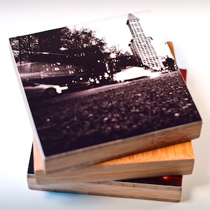 Könnte beinhalten: Ein Schwarzweißfoto einer Stadtkulisse mit einem hohen Gebäude in der Mitte. Das Foto ist auf einem Holzblock gedruckt, der auf zwei weiteren Holzblöcken gestapelt ist.