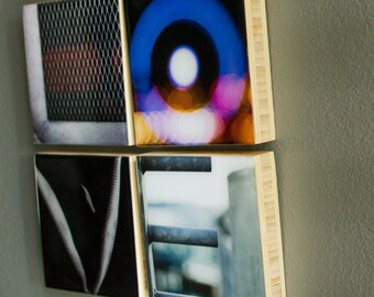 May include: A set of four square wooden tiles with images printed on them. The tiles are arranged to spell the word "LOVE". The first tile has a black and white image of a metal grate. The second tile has a colorful image of a blurred circle of light. The third tile has a black and white image of a textured surface. The fourth tile has a blurry image of a metal railing.