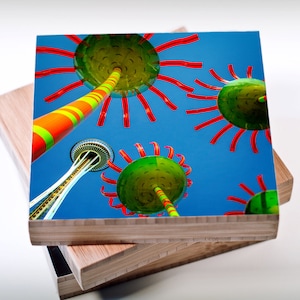 May include: A colorful abstract art print featuring a bright green and yellow striped pole with red arms extending out, against a blue sky. The Space Needle is visible in the background.