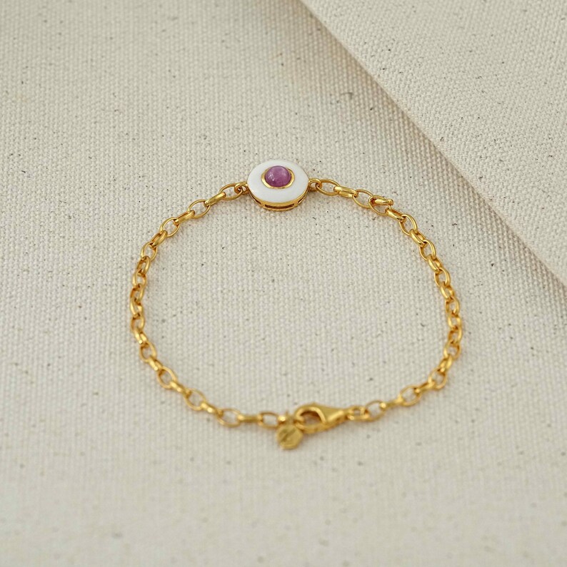 Puede incluir: Pulsera de cadena dorada con un c&iacute;rculo de esmalte blanco con una peque&ntilde;a gema rosa redonda en el centro. La pulsera tiene un dise&ntilde;o de cadena delicado y un cierre seguro.
