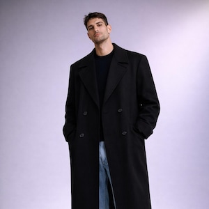 Könnte beinhalten: Ein langer, schwarzer, doppelreihiger Mantel. Der Mantel hat ein klassisches Design mit fallendem Revers und zwei Knopfreihen. Die Person trägt blaue Jeans und schwarze Schuhe. Der Mantel ist einfarbig.