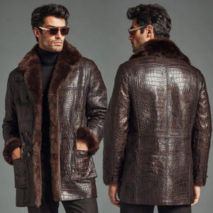 Peut inclure: Un manteau en cuir marron avec une texture peau de crocodile, avec un col et des poignets en fourrure. Le manteau a un design croisé avec deux poches avant. Le modèle porte des lunettes de soleil et un col roulé noir.