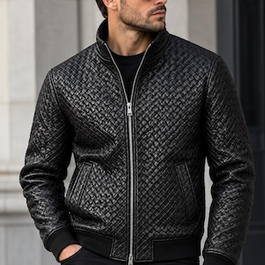 May include: A black jacket featuring a woven texture pattern, a high collar, and a silver-toned front zipper closure. The garment includes black ribbed cuffs and a matching ribbed hem, paired with a black shirt and black trousers.