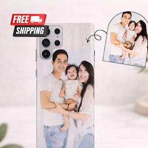 Puede incluir: Una funda de teléfono inteligente con un retrato familiar. La funda muestra una foto de una familia sonriente de tres, con una imagen más pequeña de la misma familia. La funda tiene una textura de veta de madera clara.