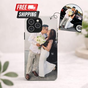 Puede incluir: Funda de teléfono inteligente con una foto personalizada de una pareja besándose, con un ramo de flores blancas. La funda tiene un módulo de cámara negro y una pancarta de envío gratuito.