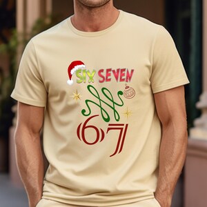 May include: A beige t-shirt with a festive design. The shirt features the words "SIX SEVEN" in red, green, and yellow, with a Santa hat on the "SIX". Below are the numbers "6 7" in red, with green swirls and gold stars.