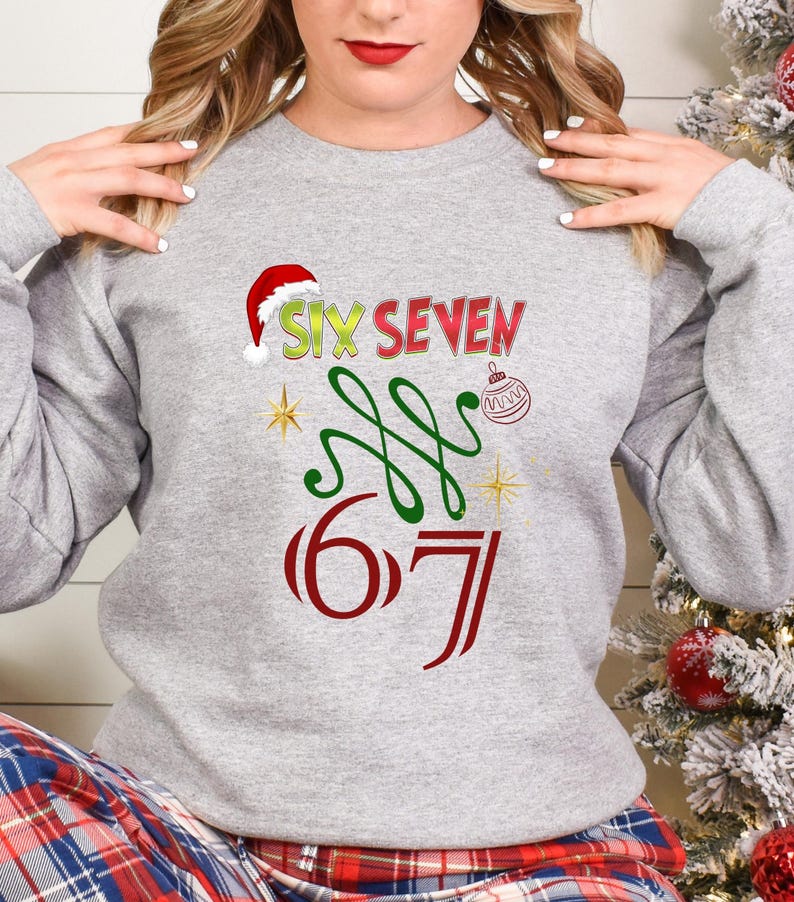 May include: A light gray sweatshirt with a festive Christmas design. The design includes the words "SIX SEVEN" in red and green, a Santa hat, a Christmas ornament, and the numbers "6 7".