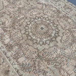 May include: A vintage-style rug with an intricate floral pattern in shades of beige, brown, and muted green. The central design features a medallion shape, surrounded by detailed botanical motifs. The rug's aged appearance adds to its classic appeal.