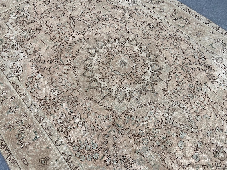 May include: A vintage-style rug with an intricate floral pattern in shades of beige, brown, and muted green. The central design features a medallion shape, surrounded by detailed botanical motifs. The rug's aged appearance adds to its classic appeal.