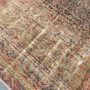 May include: An antique rug with a distressed, faded appearance. The rug features a complex, traditional pattern in shades of red, brown, beige, and blue. The edges are bordered with a detailed design.