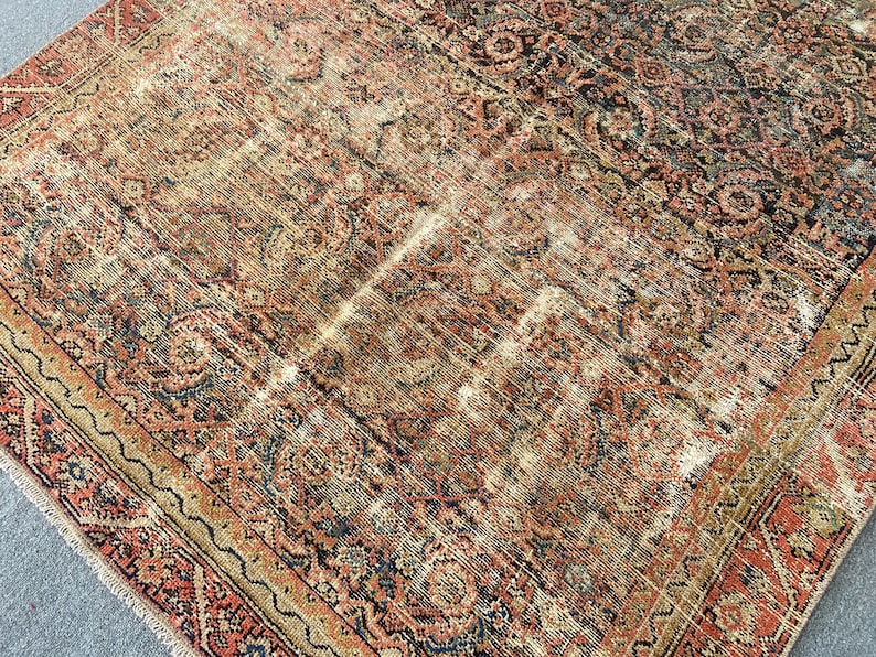 May include: An antique rug with a distressed, faded appearance. The rug features a complex, traditional pattern in shades of red, brown, beige, and blue. The edges are bordered with a detailed design.