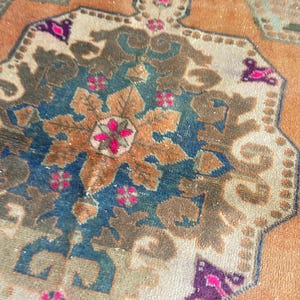 May include: A woven rug featuring a central octagonal medallion in shades of deep blue, tan, and brown. The design includes intricate floral motifs and geometric patterns in vibrant magenta, accented by a warm orange and beige background field.