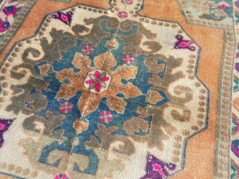 May include: A woven rug featuring a central octagonal medallion in shades of deep blue, tan, and brown. The design includes intricate floral motifs and geometric patterns in vibrant magenta, accented by a warm orange and beige background field.