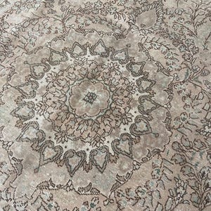 May include: Close-up of a vintage rug with a detailed floral pattern. The rug features a central medallion design in shades of brown, beige, and light green. The intricate pattern is visible across the entire surface, creating a textured appearance.